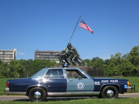1991 Ford LTD Crown Victoria - blue-and-gray Massachusetts State Police Ford sedan, unit 90E, parked on a grassy path with the Iwo Jima Memorial behind.