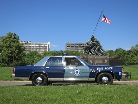 1991 Ford LTD Crown Victoria - blue-and-gray Massachusetts State Police Ford sedan, unit 90E, parked on grass with the Iwo Jima Memorial and U.S. flag behind.