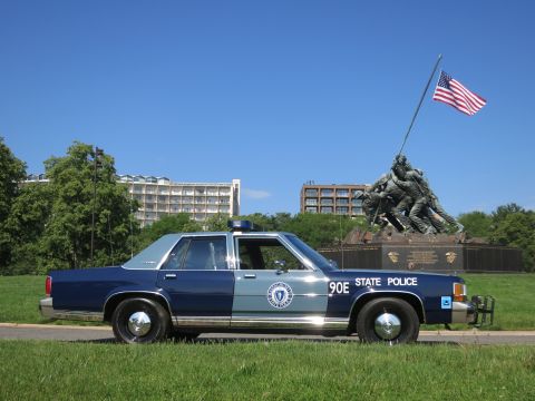 1991 Ford LTD Crown Victoria - blue-and-gray Massachusetts State Police Ford sedan, unit 90E, parked on grass with the Iwo Jima Memorial in the background.