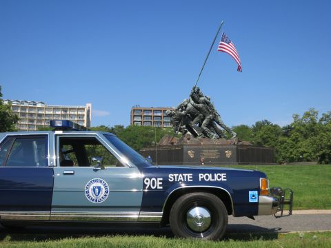 1991 Ford LTD Crown Victoria - Front-quarter view of a blue-and-gray Massachusetts State Police Ford sedan, unit 90E, parked before the Iwo Jima Memorial.