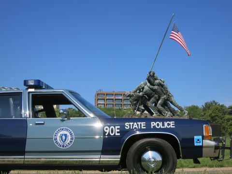 1991 Ford LTD Crown Victoria - Close rear-quarter view of a Massachusetts State Police Ford sedan, unit 90E, with door seal visible and the Iwo Jima Memorial behind.