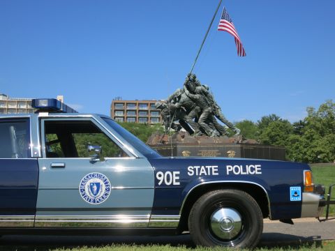 1991 Ford LTD Crown Victoria - Close front-quarter view of a Massachusetts State Police Ford sedan, unit 90E, with the Iwo Jima Memorial and U.S. flag behind.