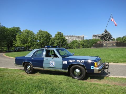 1991 Ford LTD Crown Victoria - blue-and-gray Massachusetts State Police Ford sedan, unit 90E, with a push bar, parked on grass near the Iwo Jima Memorial.