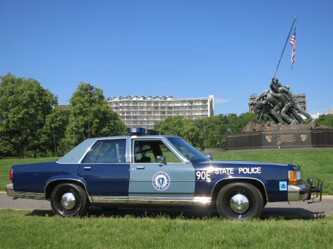 1991 Ford LTD Crown Victoria - Side view of a blue-and-gray Massachusetts State Police Ford sedan, unit 90E, with a push bar, parked before the Iwo Jima Memorial.