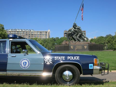 1991 Ford LTD Crown Victoria - Close side view of a Massachusetts State Police Ford sedan, unit 90E, with a push bar, parked before the Iwo Jima Memorial.