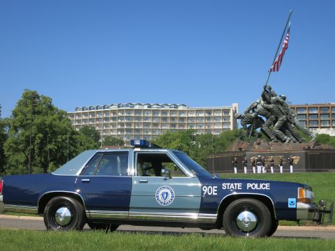 1991 Ford LTD Crown Victoria - navy and light-blue State Police cruiser with a front push bar parked before the Marine Corps flag-raising memorial.