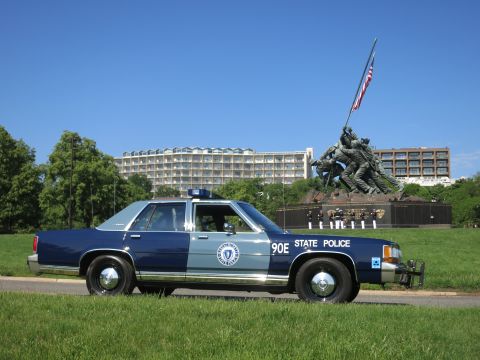 1991 Ford LTD Crown Victoria - Rear-quarter view of a Massachusetts State Police sedan marked 90E with the Marine Corps War Memorial in the background.