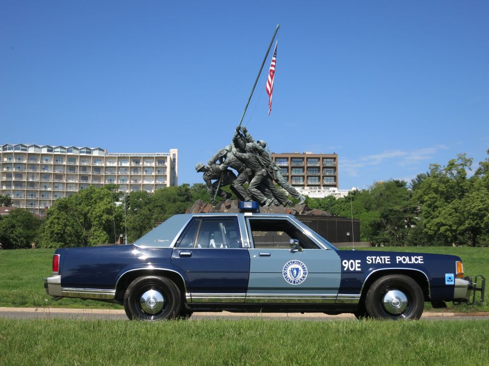 Side profile of blue Massachusetts State Police 90E sedan framed by the Iwo Jima Memorial