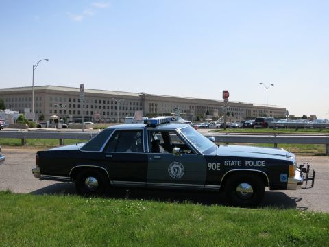 1991 Ford LTD Crown Victoria - dark two-tone Massachusetts State Police sedan marked 90E parked along a roadway with the Pentagon building behind it.