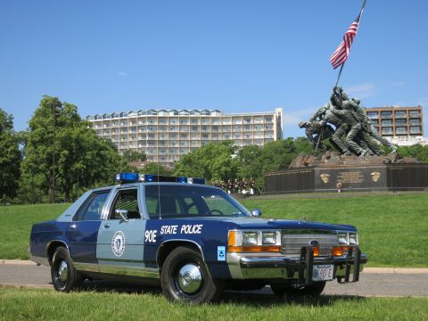 1991 Ford LTD Crown Victoria - Front three-quarter of a two-tone blue Ford State Police cruiser with a front plate, parked before the Marine memorial.