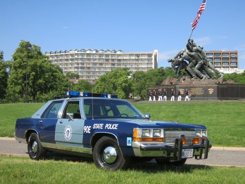 1991 Ford LTD Crown Victoria - two-tone blue State Police cruiser with brush guard before the Marine memorial, with uniformed personnel lined up behind.