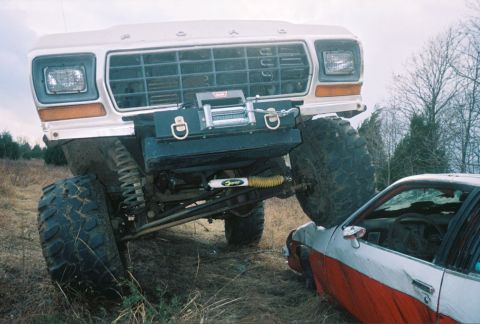 1978 Ford Bronco - A heavily modified Ford truck is positioned over a sedan, with a winch mounted on the front.