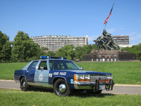 1991 Ford LTD Crown Victoria - navy and light-blue State Police sedan with brush guard parked on a lawn in front of the Marine Corps War Memorial.