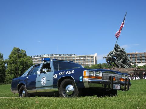 1991 Ford LTD Crown Victoria - Front three-quarter view of a two-tone blue State Police cruiser with front plate and brush guard before the Marine memorial.