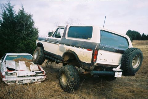 1978 Ford Bronco - A lifted 1978 Ford Bronco is positioned over a heavily damaged car in an outdoor, rural setting.