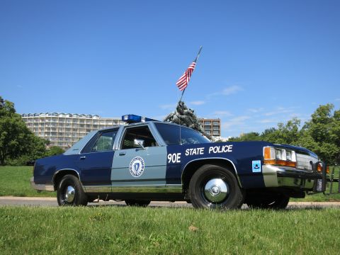 1991 Ford LTD Crown Victoria - two-tone blue Massachusetts State Police cruiser marked 90E parked at the roadside with the Iwo Jima Memorial behind it.