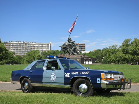 1991 Ford LTD Crown Victoria - two-tone blue Massachusetts State Police sedan marked 90E with a front push bar, parked on grass before the Iwo Jima Memorial.