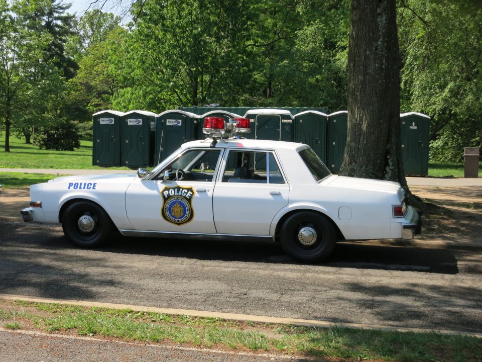 White Police sedan with light bar parked before portable toilets