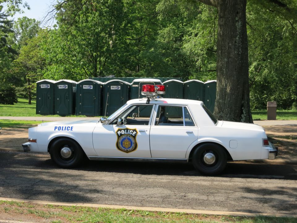 White Police sedan with light bar parked by portable toilets