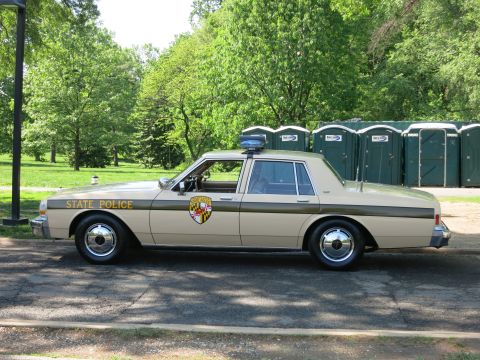1991 Ford LTD Crown Victoria - Side view of a tan two-tone State Police sedan with a gold-and-black shield emblem and rooftop light bar parked on pavement.