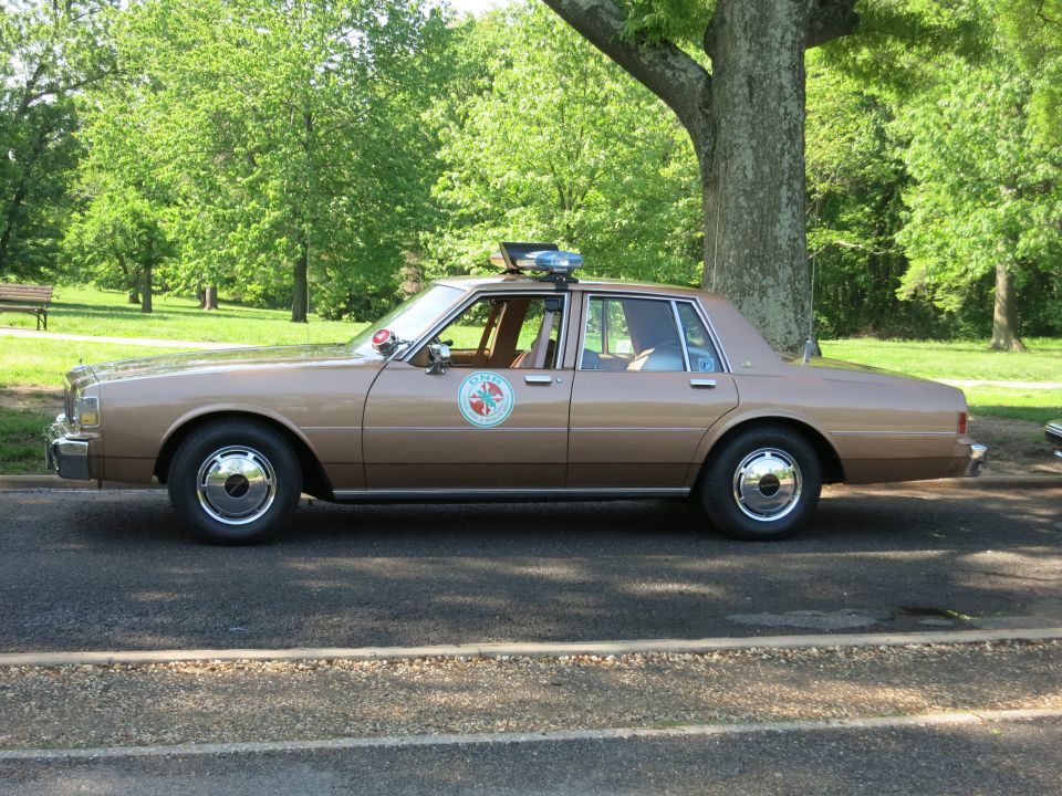 Brown two-tone sedan with circular door emblem and rooftop beacon