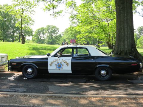 1991 Ford LTD Crown Victoria - Side view of a black and white Highway Patrol sedan with a gold star door emblem and rooftop beacon parked beside a large tree.