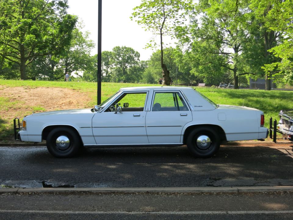 White Ford LTD Crown Victoria four-door sedan parked in profile by a park lawn
