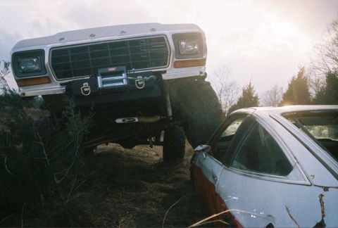 1978 Ford Bronco - A large Ford truck looms over a smaller car in an outdoor setting.