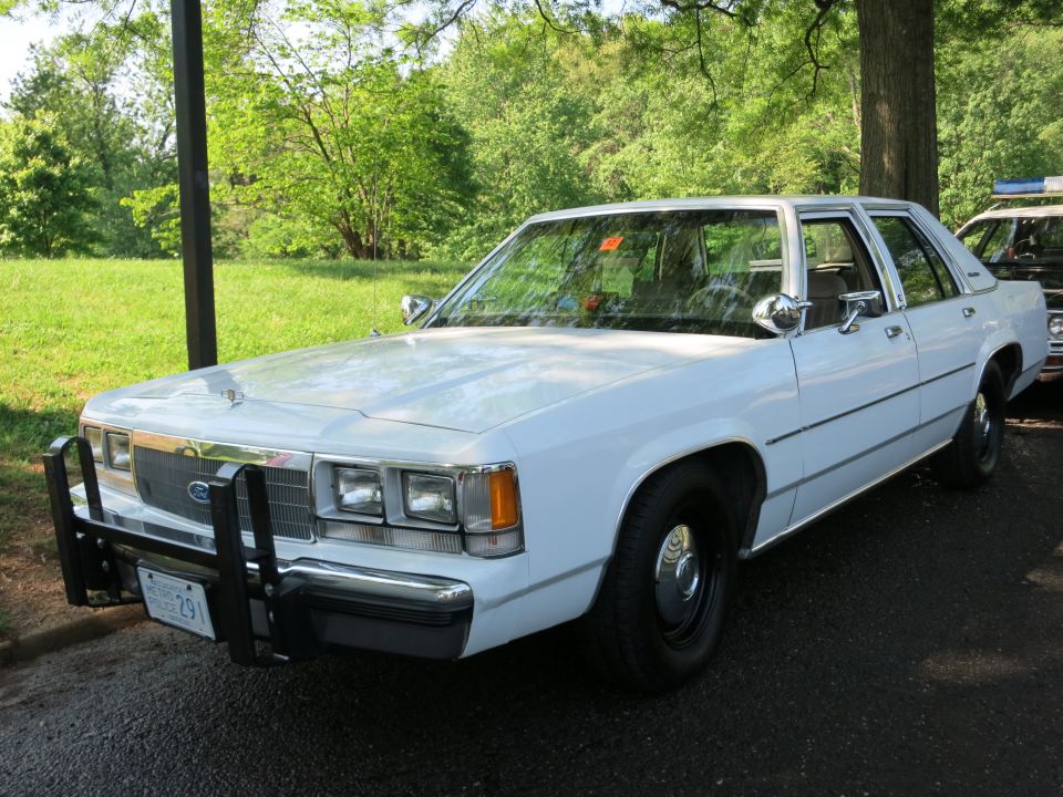 Black and white Highway Patrol coupe with light bar leading a line of cars