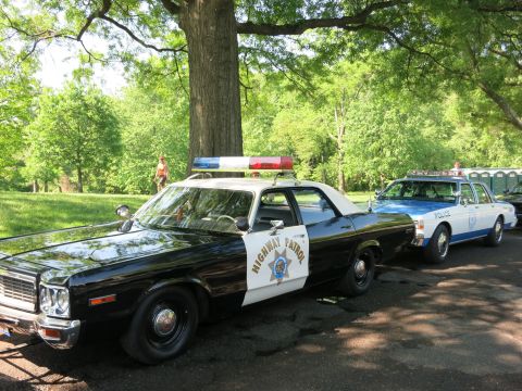 1991 Ford LTD Crown Victoria - blue-and-white police sedan marked '334-2424' parked in front of a Norfolk Christian Schools bus near office buildings.
