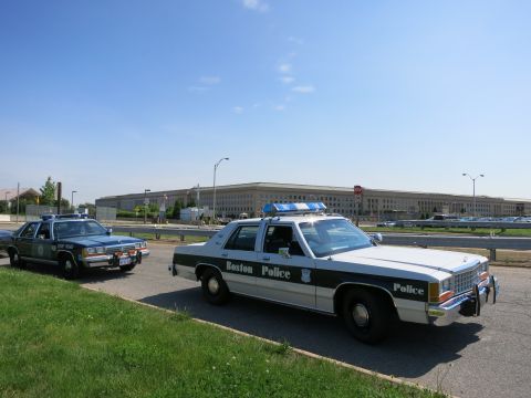 1991 Ford LTD Crown Victoria - Two black-and-white Boston Police Ford cruisers parked in front of the long Pentagon building under blue sky.