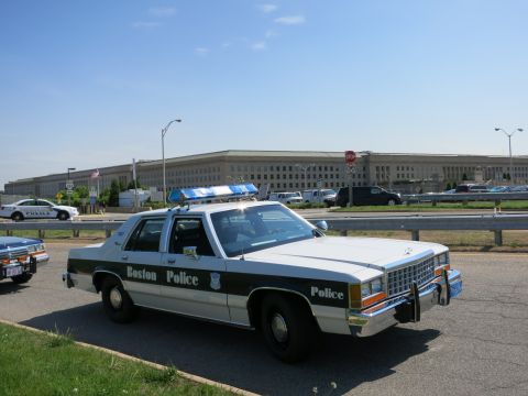 1991 Ford LTD Crown Victoria - black-and-white Boston Police Ford cruiser and other police cars parked in front of the Pentagon under blue sky.