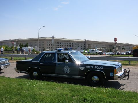 1991 Ford LTD Crown Victoria - dark and gray State Police Ford sedan marked 90E with chrome push bar and roof lightbar parked before the Pentagon.