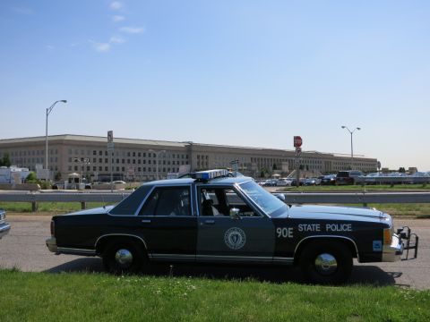 1991 Ford LTD Crown Victoria - Profile view of a black and gray State Police Ford sedan numbered 90E parked on grass in front of the Pentagon.