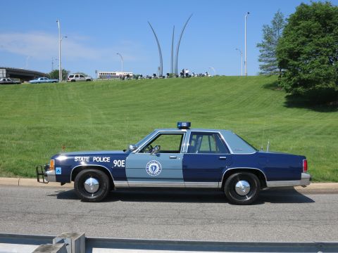 1991 Ford LTD Crown Victoria - two-tone blue State Police Ford sedan numbered 90E parked on a road with the Air Force Memorial spires rising over the green hill.