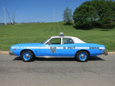 1991 Ford LTD Crown Victoria - light blue and white 'Police 5 PCT 2655' sedan with NYPD-style shield emblem parked on a road below a grassy hill.