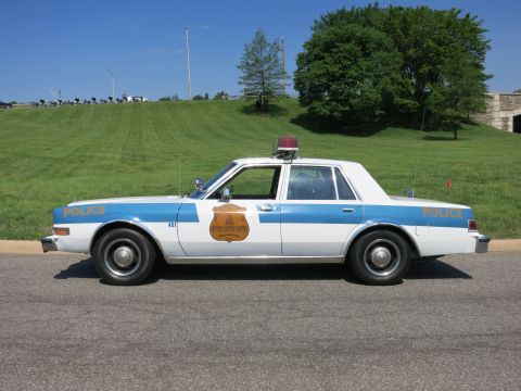 1991 Ford LTD Crown Victoria - tan and brown 'State Police' Chevrolet sedan with Maryland-style shield door emblem and roof light parked on a road.