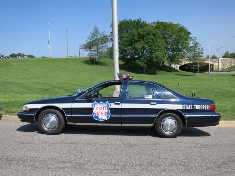 1991 Ford LTD Crown Victoria - dark blue and white Chevrolet Caprice marked 'State Trooper' with a 'State Patrol' shield on the door, parked on a road.