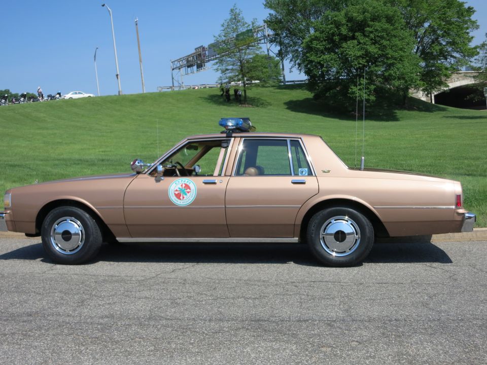 Tan brown police Chevrolet Caprice sedan with round door emblem and roof lights