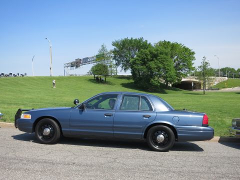 1991 Ford LTD Crown Victoria - dark blue Ford Crown Victoria sedan with black steel wheels and push bar sits parked on a road beside a green hill.