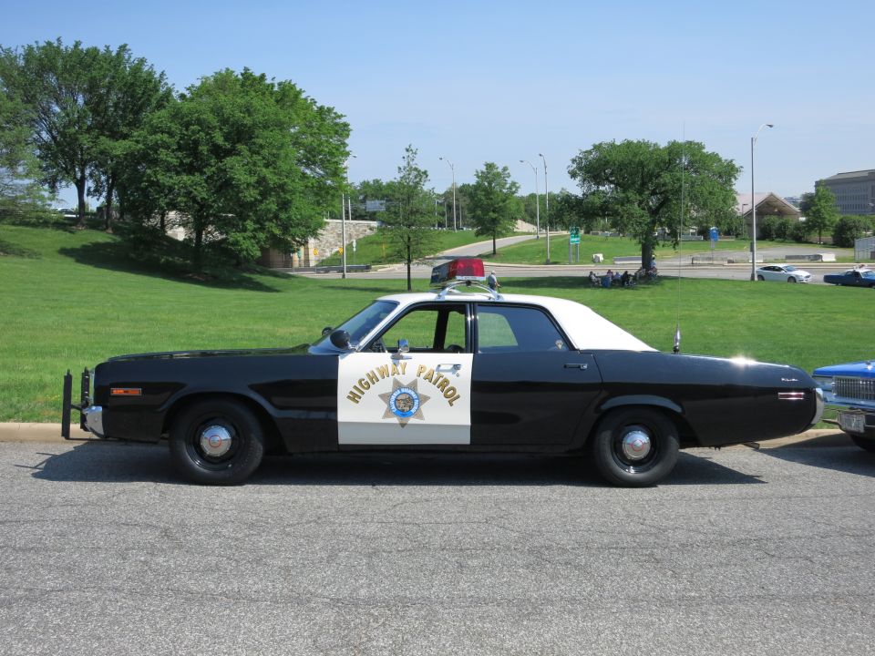 Black and white HIGHWAY PATROL sedan with star shield, parked by a grassy slope