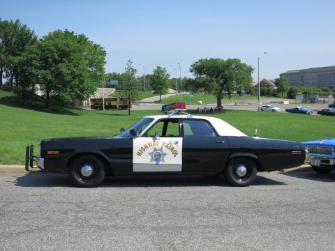 1991 Ford LTD Crown Victoria - black-and-white Highway Patrol sedan with a white roof and gold star door emblem sits parked on pavement near trees.