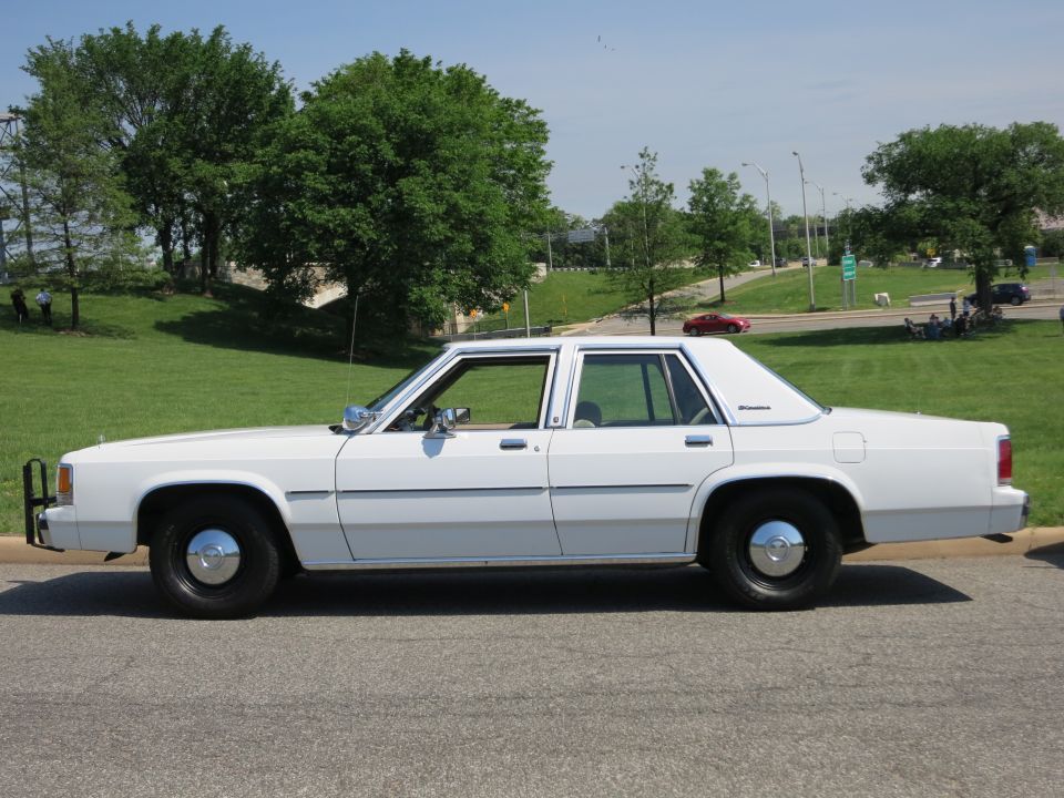 White Ford LTD Crown Victoria police-style sedan with push bar and black wheels, parked roadside