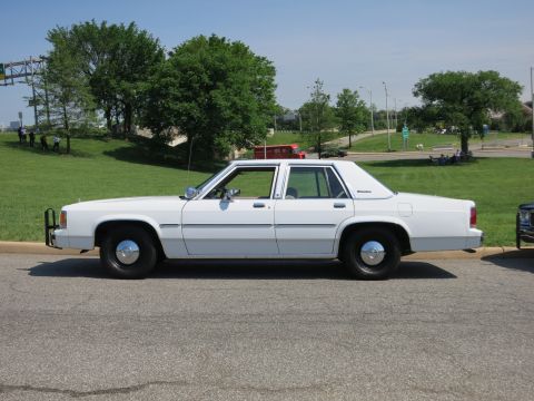 1991 Ford LTD Crown Victoria - white Ford LTD Crown Victoria sedan with a front push bar and black wheels sits parked roadside under blue sky.
