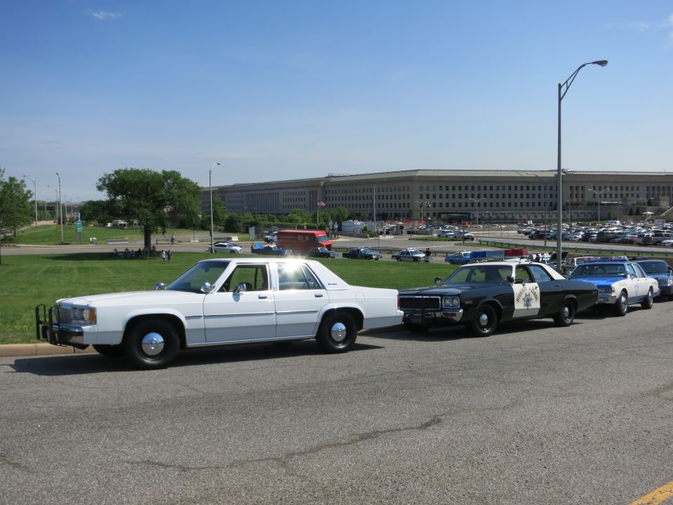 Row of vintage police cars parked in front of the Pentagon under blue sky