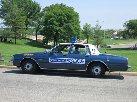 1991 Ford LTD Crown Victoria - dark blue North Haven Police Supervisor sedan numbered 13 with a white roof and roof beacon is parked beside a grassy hill.