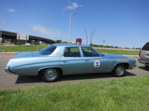 1991 Ford LTD Crown Victoria - light blue four-door police sedan marked POLICE sits on a roadside strip of grass near an overpass.