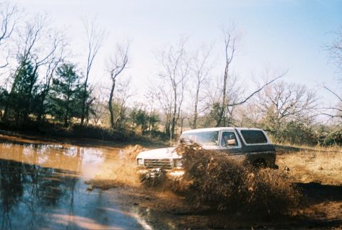 1978 Ford Bronco - Ford Bronco navigating a muddy trail, kicking up a large spray.