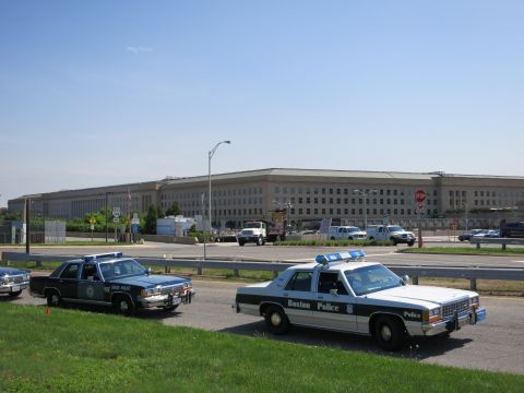 1991 Ford LTD Crown Victoria - Vintage State Police and Boston Police cruisers sit on a road before a long stone government building and parking area.