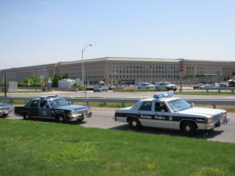 1991 Ford LTD Crown Victoria - dark State Police cruiser and a Boston Police cruiser are parked on grass in front of a long stone government building.